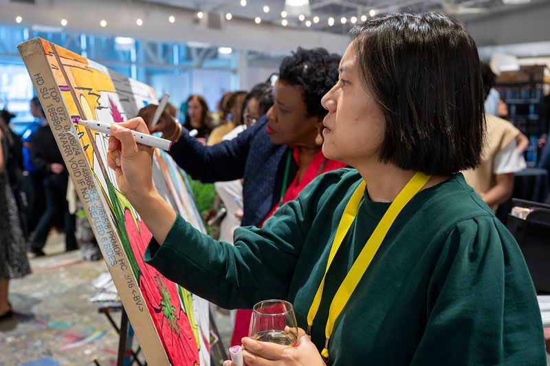 An attendee paints on a collaborative art canvas during a GEO conference while other attendees contribute in the background.